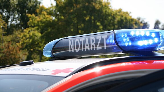 Nahaufnahme eines Rettungswagens: blaues Blaulicht mit Schriftzug „NOTARZT“ auf dem Fahrzeugdach, aktiv.