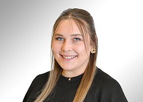 Franziska Rost Porträtfoto: Eine lächelnde Frau blickt in die Kamera. Lange, dunkelblonde Haare, Nasenpiercing, goldene Ohrringe, schwarze Oberbekleidung, zarte Kette. Neutraler, heller Hintergrund. Fokus auf freundlichen, professionellen Ausdruck.