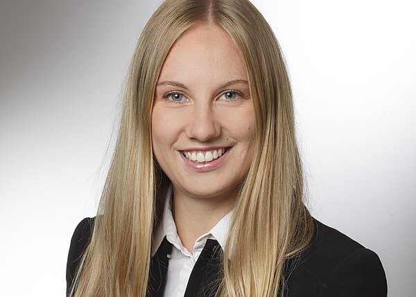 Porträtfoto: Eine lächelnde Frau mit langen blonden Haaren blickt in die Kamera. Sie trägt einen schwarzen Blazer über weißem Hemd. Neutraler, heller Hintergrund; klassisches Bewerbungs- oder Businessfoto.
