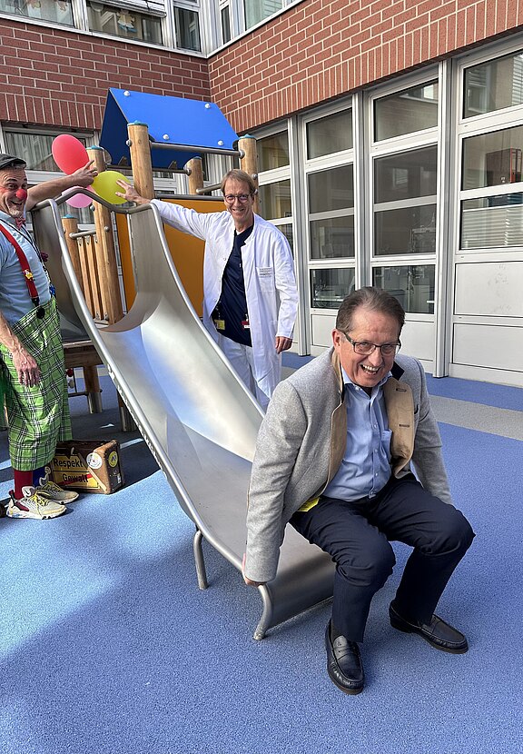 Das Bild zeigt Dietmar Pawlik, Geschäftsführer der Klinikum Bayreuth GmbH, beim Rutschen anlässlich der Einweihung des neuen Spielplatzes der Kinderklinik.