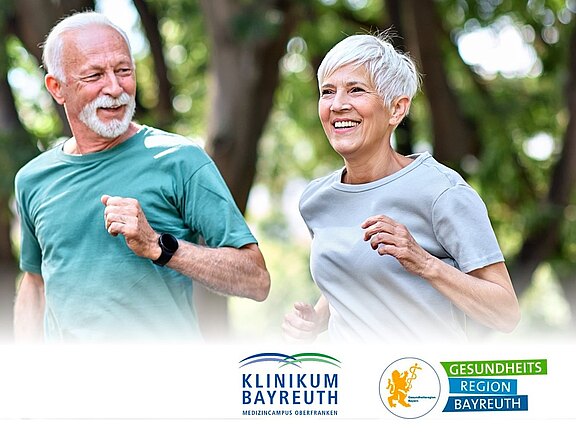 Zwei ältere Erwachsene joggen lächelnd im Park, beide in Sportkleidung. Sonnenlicht und Bäume im Hintergrund betonen eine entspannte Outdoor-Bewegung. Das Bild steht für Aktivität, Gesundheit und Lebensfreude im Alter.