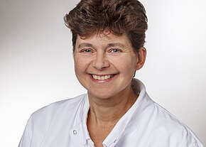 Dr. med. Michaela Wienziers Porträt einer lächelnden erwachsenen Person mit kurzem Haar in weißem Arztkittel vor neutralem Hintergrund; Kopf-und-Schultern-Aufnahme.