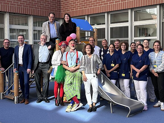Das Bild zeigt das Team der Kinderklinik gemeinsam mit Geschäftsführer Dietmar Pawlik, Baudirektorin Sonja Pöhlmann, Landrat Florian Wiedemann, Oberbürgermeiter Thomas Ebersberger bei der Eröffnung des Spielplatzes im Innenhof der Kinderklinik vor einem neuen Spielturm.