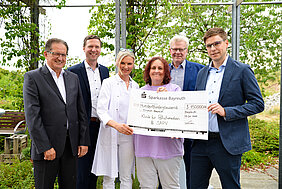 Eine Gruppe von fünf Personen steht im Freien und hält einen großen Scheck der Sparkasse Bayreuth über 150.000 Euro. Der Scheck ist für die Klinik für Palliativmedizin und SAPV bestimmt. Das Datum auf dem Scheck ist der 3. Juli 2023.