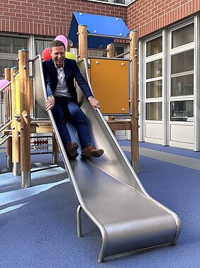 Das Bild zeigt Landrat Florian Wiedemann beim Rutschen bei der Einweihung des neuen Spielplatzes in der Kinderklinik am Klinikum Bayreuth. 
