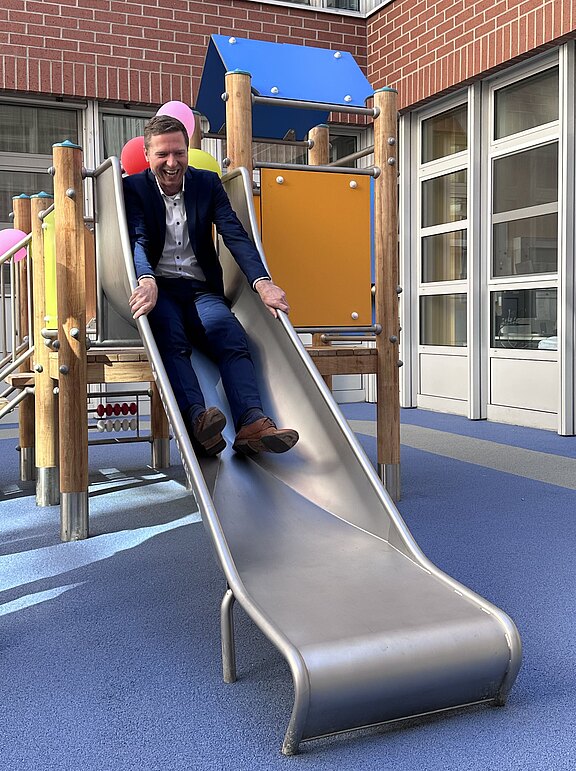Das Bild zeigt Landrat Florian Wiedemann beim Rutschen bei der Einweihung des neuen Spielplatzes in der Kinderklinik am Klinikum Bayreuth.