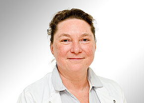 Porträtfoto einer lächelnden Person in weißem Arztkittel vor hellem, neutralem Hintergrund; direkter Blick in die Kamera, freundlicher Ausdruck.