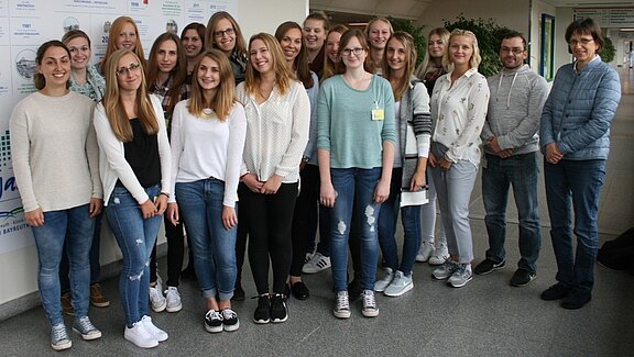 Gruppenfoto: Eine größere Gruppe von Personen steht eng zusammen in einem Flur und lächelt in die Kamera; Fokus auf dem gemeinsamen Auftreten der Gruppe.
