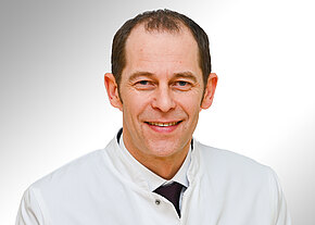 Prof. Dr. med. Alexander Link Porträt eines lächelnden Mannes mittleren Alters in weißem Arztkittel vor neutralem Hintergrund; er blickt direkt in die Kamera.