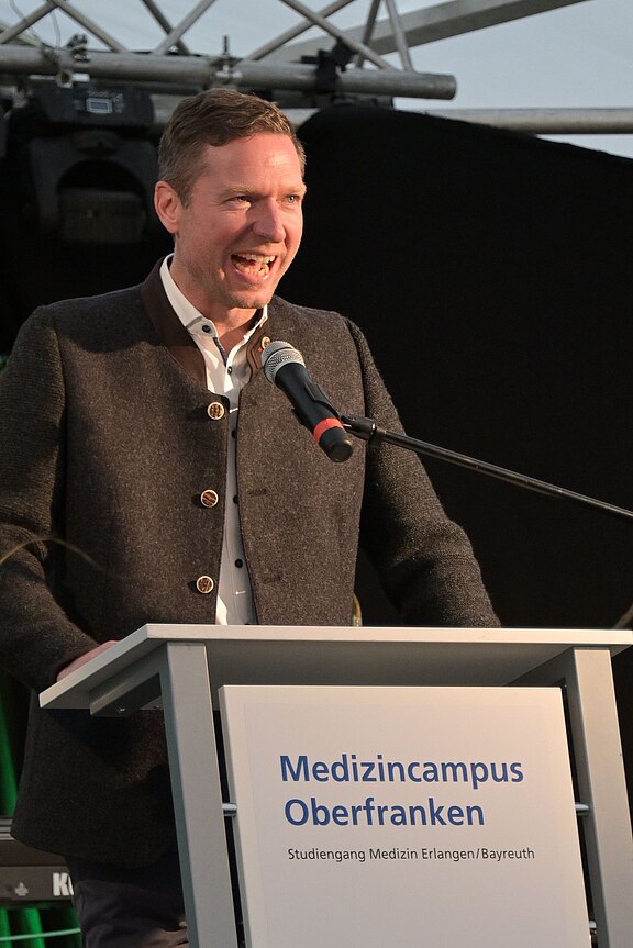 Ein Mann spricht engagiert ins Mikrofon an einem Rednerpult. Auf dem Pult steht: „Medizincampus Oberfranken – Studiengang Medizin Erlangen/Bayreuth.“