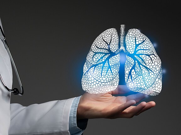 Eine Person im Arztkittel hält eine leuchtende, holografische Darstellung von Lungen mit sichtbaren Bronchien über der geöffneten Hand. Das Motiv symbolisiert Atemwegsdiagnostik, Lungenmedizin oder Gesundheitstechnologie auf dunklem Hintergrund.