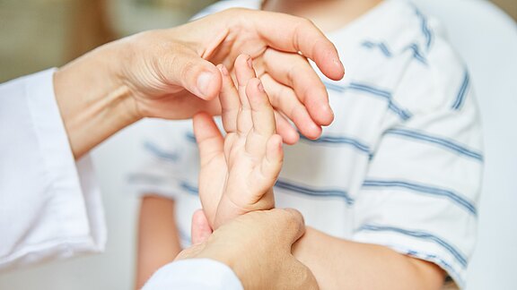 Nahaufnahme: Eine erwachsene Hand untersucht behutsam die Handfläche eines Kindes – symbolisiert medizinische Untersuchung, Betreuung oder Therapie. Fokus auf Berührung und Fürsorge.