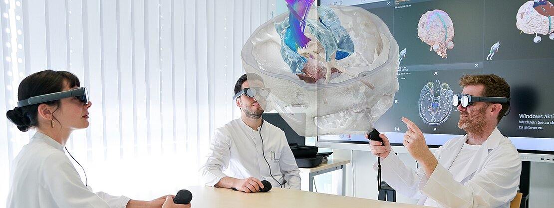 OP-Planung: Eine Ärztin, ein Arzt und Prof. Stefan Linsler aus der Klinik für Neurochirurgie blicken durch VR-Brillen auf das raumfüllende Modell eines menschlichen Gehirns.