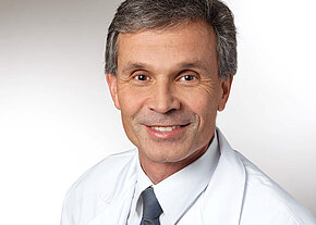 Prof. Dr. med. Harald Rupprecht Porträt eines lächelnden Mannes mittleren Alters in weißem Arztkittel und Krawatte vor neutralem Hintergrund; professioneller, freundlicher Ausdruck.