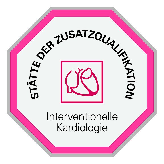Das Bild zeigt ein oktagonales Schild mit dem Text „Stätte der Zusatzqualifikation“ und „Interventionelle Kardiologie“. In der Mitte befindet sich eine rote Grafik eines Herzens.