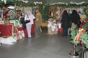 Ein Weihnachtsmarkt mit dekorativen Ständen, die mit festlichen Produkten geschmückt sind. Menschen sehen sich die Angebote an, während Weihnachtsdekoration die Umgebung ziert. Die Atmosphäre ist gemütlich und einladend.