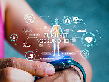 Eine Person betrachtet ein modernes Fitnessarmband. Über dem Armband sind digitale Gesundheitsdaten und grafische Darstellungen von Körperfunktionen schwebend dargestellt. Der Text "Zukunft Gesundheit" wird zentral angezeigt, was auf innovative Ansätze zur Gesundheitsüberwachung hinweist.